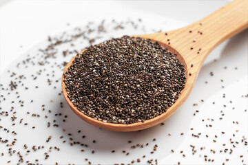 Wooden spoonful of wholesome chia seeds. Source of Omega 3 fatty acids on white ceramic surface