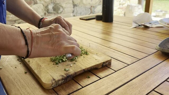 Close up shot of woman's hands cutting herbal on a wooden cutting board. 