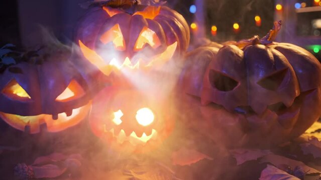 Blurred Background of 4 traditional carved jack-o'-lanterns stand among a beautifully decorated holiday backdrop with garlands and candles during a Halloween celebration in the smoke.