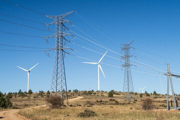 Vista de un parque eolico con una linea electrica de alta tension y aerogeneradores. - obrazy, fototapety, plakaty