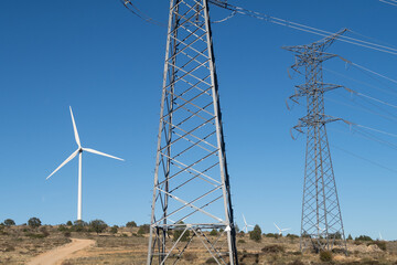 Vista de una linea electrica de alta tensión y un aerogenerador en un parque eolico. - obrazy, fototapety, plakaty