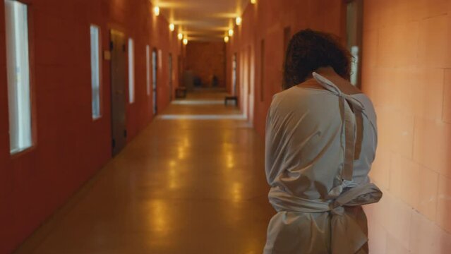 Rear view shot of unrecognizable man with mental disorder wearing straitjacket walking along corridor in asylum