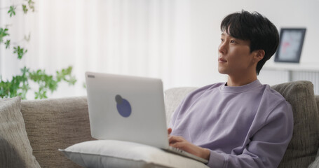 Young Handsome Asian Male Browsing Internet, Using Laptop Computer at Home, Online Shopping for...
