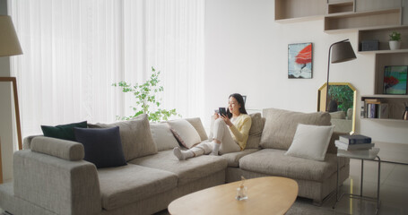 Portrait of a Pretty Korean Female Using Smartphone and Holding a Credit Card. Asian Woman Doing Mobile Retail Therapy, Browsing Online Shopping Website in a Living Room, Discovering Stylish Trends