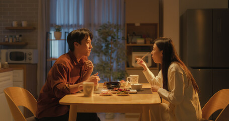 Fototapeta premium Young Loving South Korean Couple Eating Homemade Tasty Food at Home and Having a Fun Chat. Asian Boyfriend and Girlfriend Enjoying Time Together, Feasting on Cooked Meat, Spicy Vegetable Soup and Rice