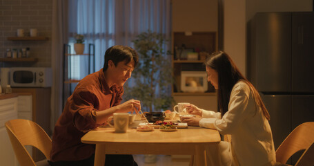 Young Loving South Korean Couple Eating Homemade Tasty Food at Home and Having a Fun Chat. Asian...
