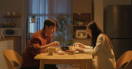 Fotobehang Young Loving South Korean Couple Eating Homemade Tasty Food at Home and Having a Fun Chat. Asian Boyfriend and Girlfriend Enjoying Time Together, Feasting on Cooked Meat, Spicy Vegetable Soup and Rice © Kitreel