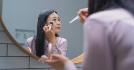 Stylish South Korean Female Using a Soft Brush to Put Tonal Foundation Cream in a Bathroom at Home....