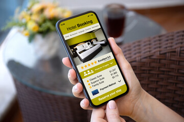 Man hand hold phone with hotel booking application background cafe