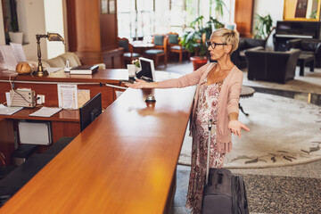 Mature woman comes to the hotel at the reception. She is tired of waiting for receptionist.