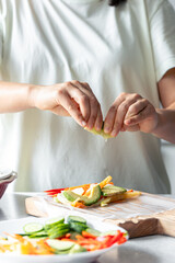 Woman preparing spring rolls in rice paper on kitchen table.