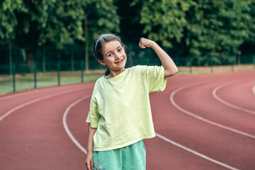 Strong little girl posing outdoors showing their muscles.