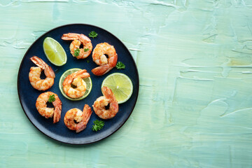 Shrimps, shot from above with a place for text on a teal blue table. Cooked shrimp with lime, tasty gourmet dish