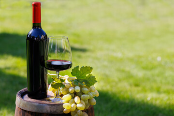 Fototapeta premium Wine bottle, red win glass and grape on barrel