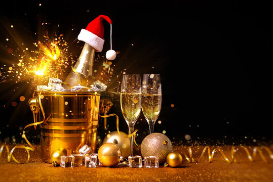 A bottle of champagne in a golden bucket with ice and two glasses of champagne on a black background in Christmas decorations.