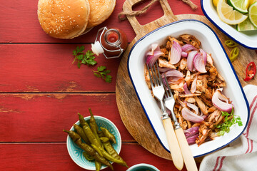 Pulled bbq chicken with baked onions on serving platter, bbq corn, pickles, chili peppers and buns for hot dogs and burgers, tomato sauce. Traditional American grilled summer bbq sandwiches dishes.