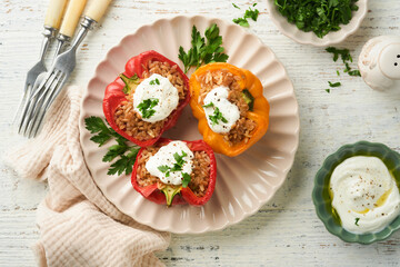 Roast stuffed red and yellow bell peppers with couscous, brown rice and spelled with Greek sauce and olive oil on rustic wooden background. Healthy dinner eating. Autumn cozy dinner concept. Top view
