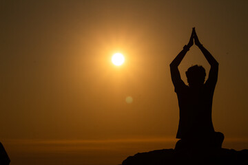 silhouette of the Young man doing yoga or meditation or praying on edge of a mountain at sunset, World yoga day