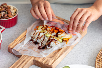 Woman preparing spring rolls in rice paper on kitchen table.