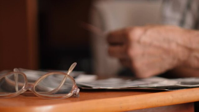 A 70-year-old pensioner is looking at old family photo archives at home, laying out the photos on the table. elderly father remembers the past, pensioner nostalgia concept