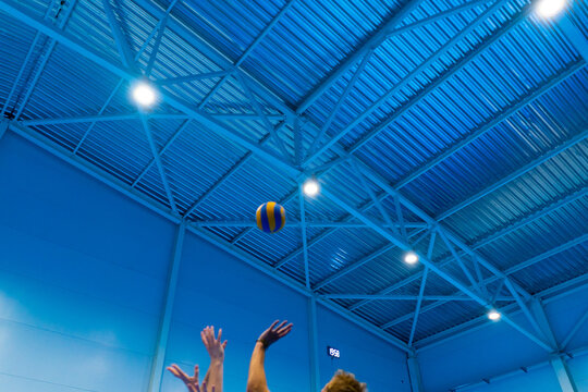 a volleyball ball in the air flies over the net and flies to a part of the opponents who are trying to repel it with their hands competition game - Powered by Adobe