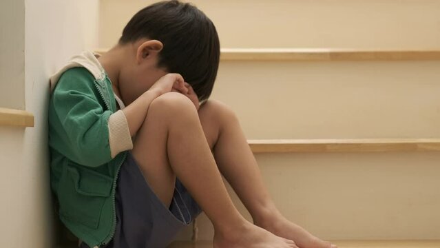 A sad Asian boy sits with his head down on the steps.