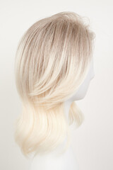 Naklejka premium Natural looking blonde fair wig on white mannequin head. Middle length hair cut on the plastic wig holder isolated on white background, side view.
