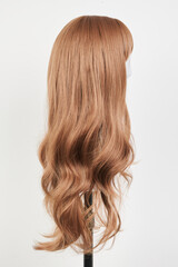 Natural looking dark blonde wig on white mannequin head. Long fair hair cut on the plastic wig holder isolated on white background