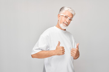 Portrait of mature man in white T-shirt and glasses smiling joyfully showing thumbs up gesture isolated on white studio background. Approves good choice, right decision.