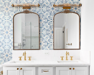 A bathroom detail with a blue and yellow pattern wallpaper, bronze mirrors and light fixtures, gold...