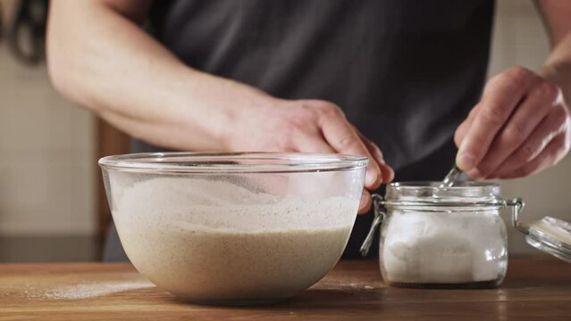 A man making poffertjes at home - adding salt to batter. Traditional Dutch mini pancakes with buckwheat flour, white flour, egg and milk.