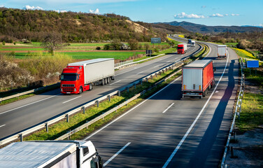 Highway transportation scene with Convoys or fleets of transportation trucks in both ways,on rural highway under a beautiful blue sky