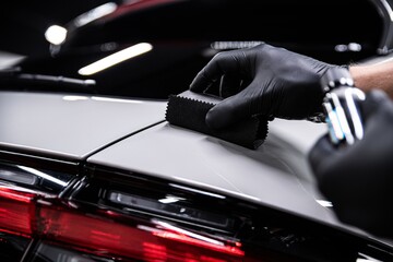 Employee of a car detailing studio or car wash applies a ceramic coating to the paint of a gray car - 655810416