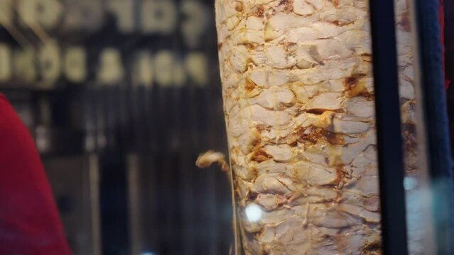 A chef skillfully cuts shawarma meat for the traditional Turkish Doner Kebab. Close-up of hands wielding a sharp knife in a dynamic street food setting.