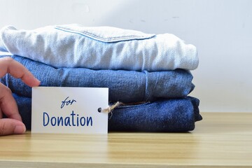 Woman hand organizing a few shades of used blue jeans on the desk with tag for donation.