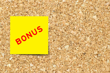 Yellow note paper with word bonus on cork board background with copy space