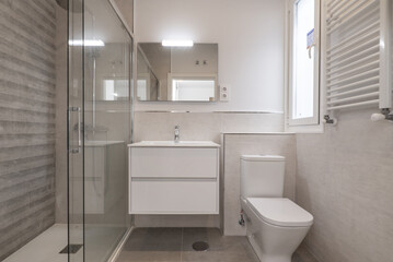 Fototapeta na wymiar A small bathroom with a white towel radiator, a white wooden hanging cabinet with a sink and a frameless mirror on the wall.