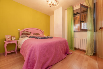 Double bedroom with pink painted wooden furniture, bedspread of the same color, wooden floor, built-in wardrobe of the same color and brown aluminum window