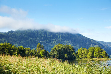 Lake Ossiacher See, Ossiach, Carinthia, Austria. Beautiful summer mountain landscape. Alpine lake surrounded by mountains, slopes of which are covered with forest and white fluffy clouds