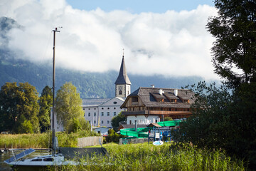 Ossiach Abbey, Lake Ossiacher See in Ossiach, Carinthia, Austria. Beautiful summer mountain landscape with church. A former Benedictine monastery and Alpine lake in mountains with white clouds - obrazy, fototapety, plakaty