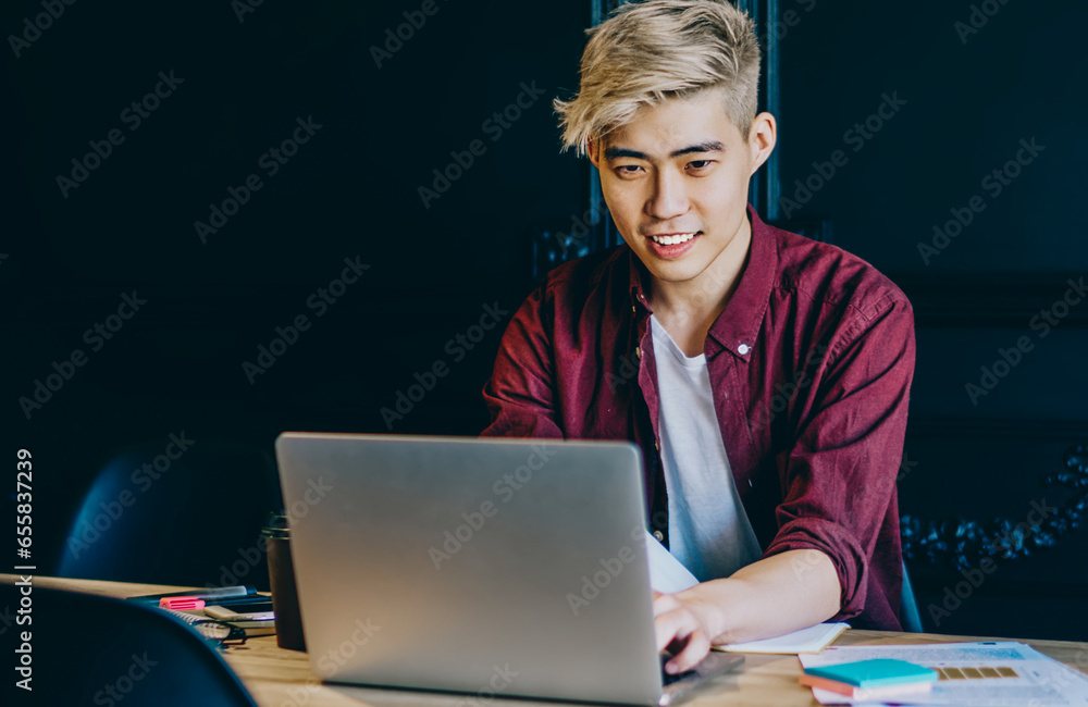 Poster positive young man chinese updating software on laptop computer using wireless internet connection