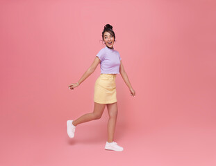 Happy Asian teen woman smiling and walking while looking back isolated on pink background.