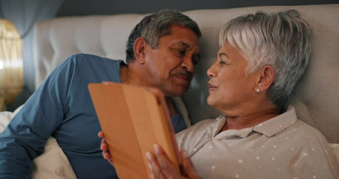 Love, kiss and senior couple in a bed with tablet for social media, streaming or ebook at home. Happy, relax and retired man with old woman in a bedroom for digital, search or chat communication