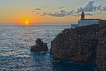 
red lighthouse at sunset on a cliff overlooking the ocean