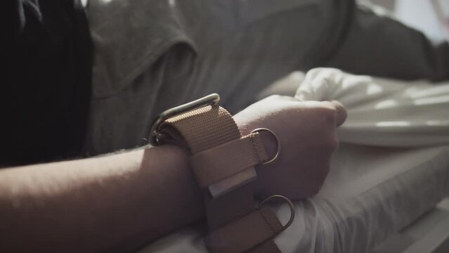 Selective focus shot unrecognizable patient with mental illness with arms tied to hospital bed with brown belts suffering seizure