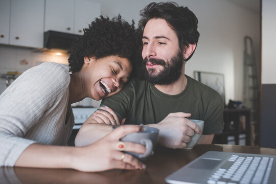 Young multiethnic couple using pc having coffee