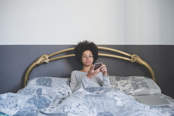 Multiethnic woman using smartphone lying bed after wake up