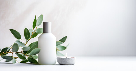 A white bottle with a silver cap , small white candle on a white surface and eucalyptus branch with green leaves. Clean and minimalistic mood.