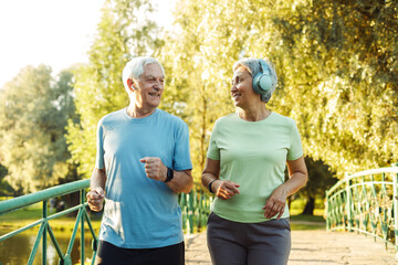 Senior mature couple running together in the park looking at each other while jogging slimming...