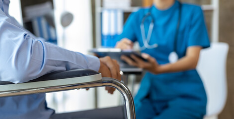 Man with a leg injury in a wheelchair sees a doctor in a hospital for a check-up. Female doctor examining a wheelchair patient in an examination room at a hospital.